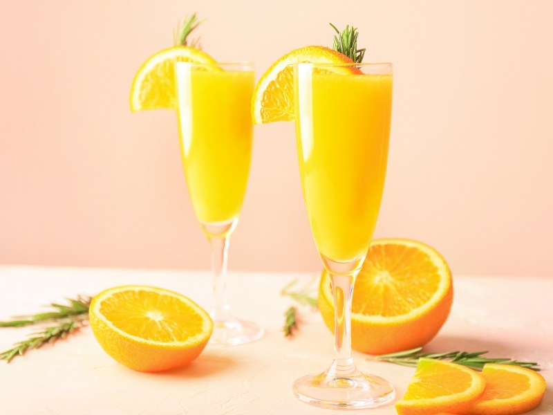 Zwei Mimosa Drinks auf einem Tisch, angeschnittene Orangen daneben.