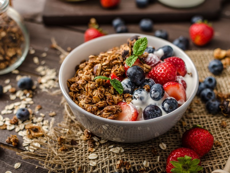 Eine SchÃ¼ssel MÃ¼sli mit Joghurt und Balsamico-Beeren, drumherum verstreut die Zutaten.