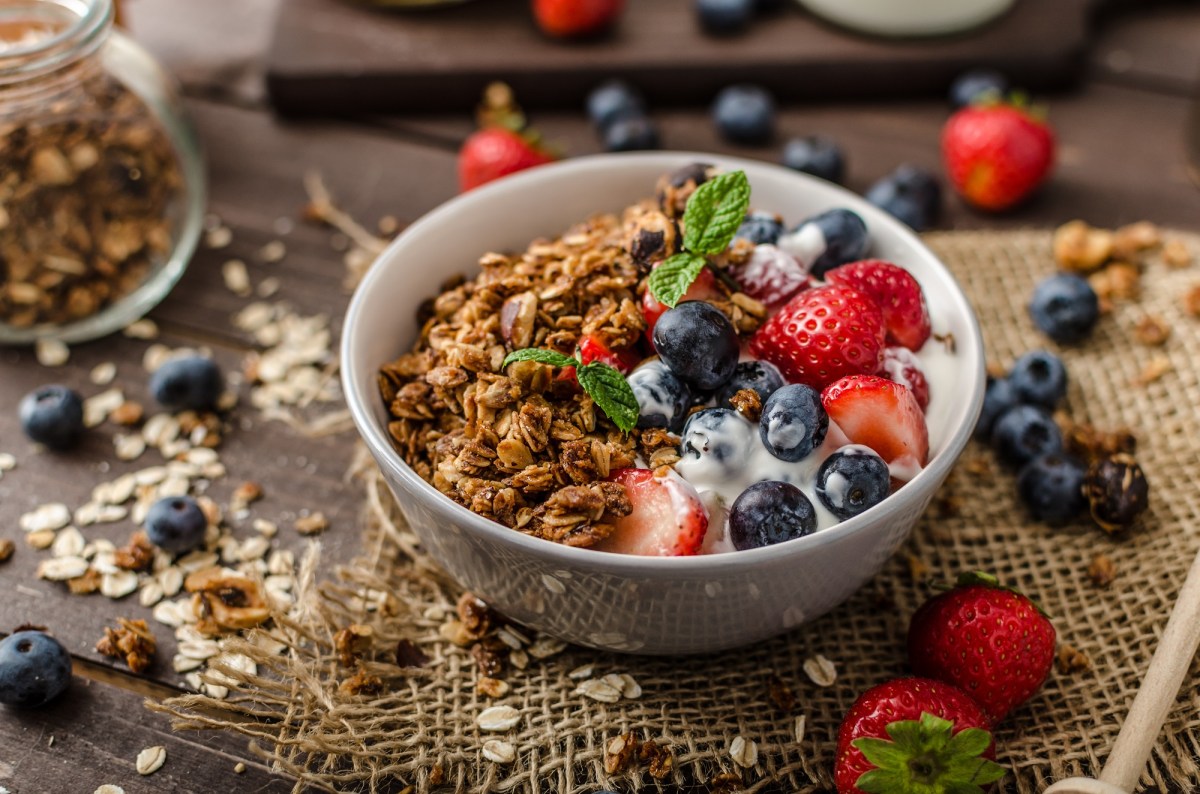 Eine SchÃ¼ssel MÃ¼sli mit Joghurt und Balsamico-Beeren, drumherum verstreut die Zutaten.