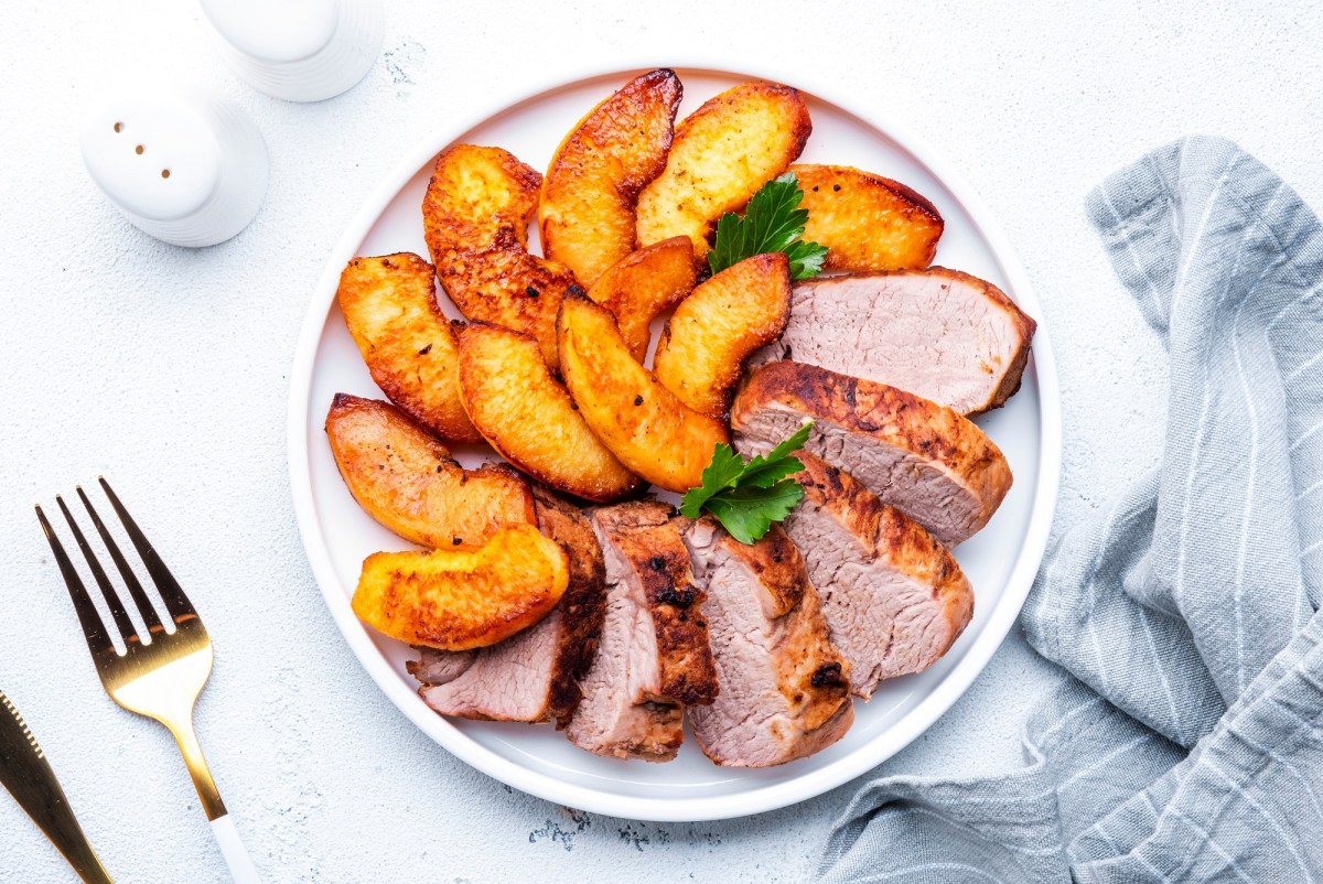 Angeschnittenes Schweinefilet mit geschmorten Ã„pfeln auf einem weiÃŸen Teller.