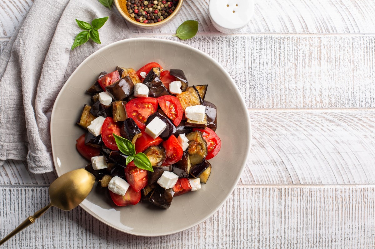 Tomatensalat mit Feta und Aubergine, angerichtet mit Basilikum, auf einem hellen Teller.