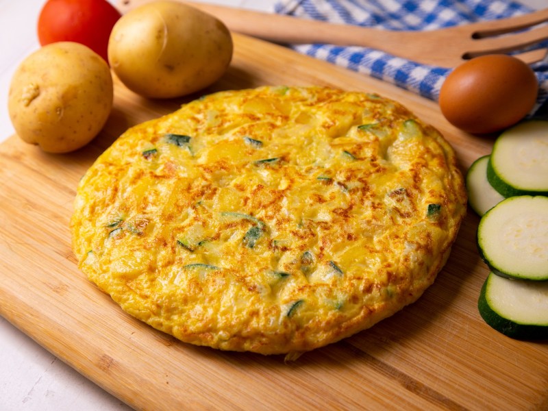 Eine Tortilla de Patata mit Zucchini auf einem Holzbrett.