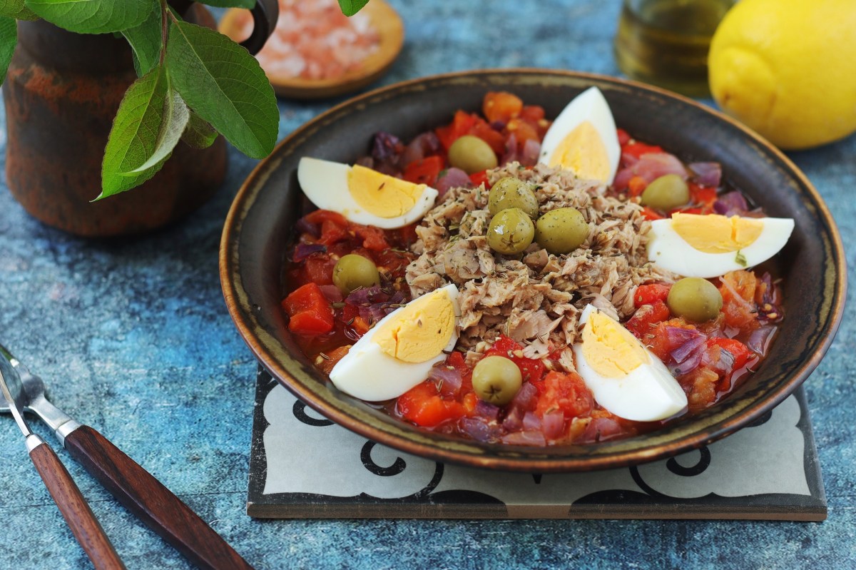 Tunesischer Grillsalat Slata Mechouia, serviert mit Thunfisch und Eiern, auf einem dunklen Teller.