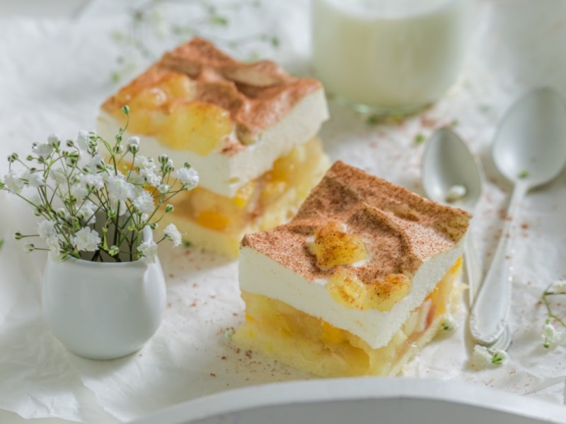 Zwei Stücke Apfel-Zimt-Torte auf einem Serviertablett. Daneben sind eine Vase mit Blumen und ein Löffel.