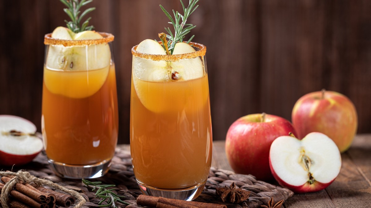 Herbst-Cocktail in zwei GlÃ¤sern, garniert mit Apfel und Rosmarin. Daneben halbierte und ganze Ã„pfel.