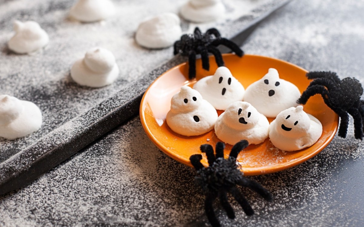 FÃ¼nf sÃ¼ÃŸe Baiser-Geister auf einem orangen Teller. Spinnen als Halloween-Deko liegen daneben.