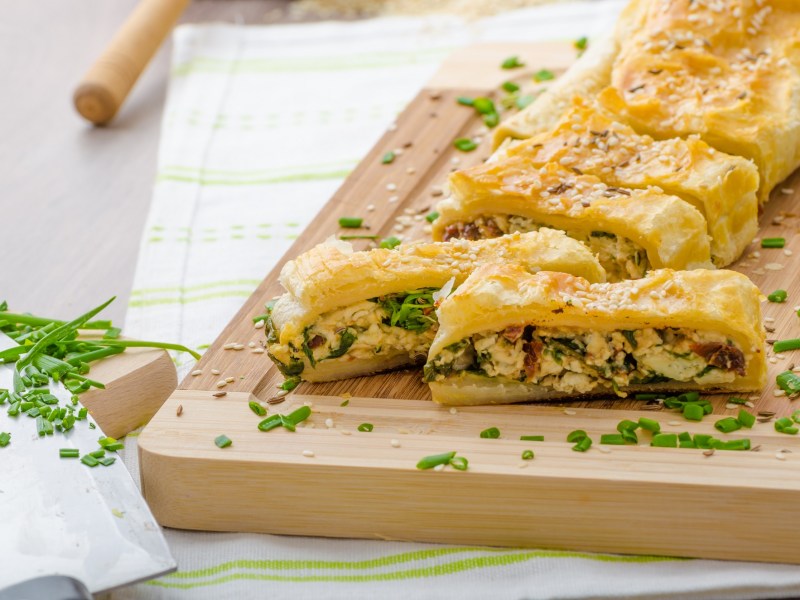 Brett mit angeschnittenem BlÃ¤tterteigstrudel mit Spinat und BlauschimmelkÃ¤se