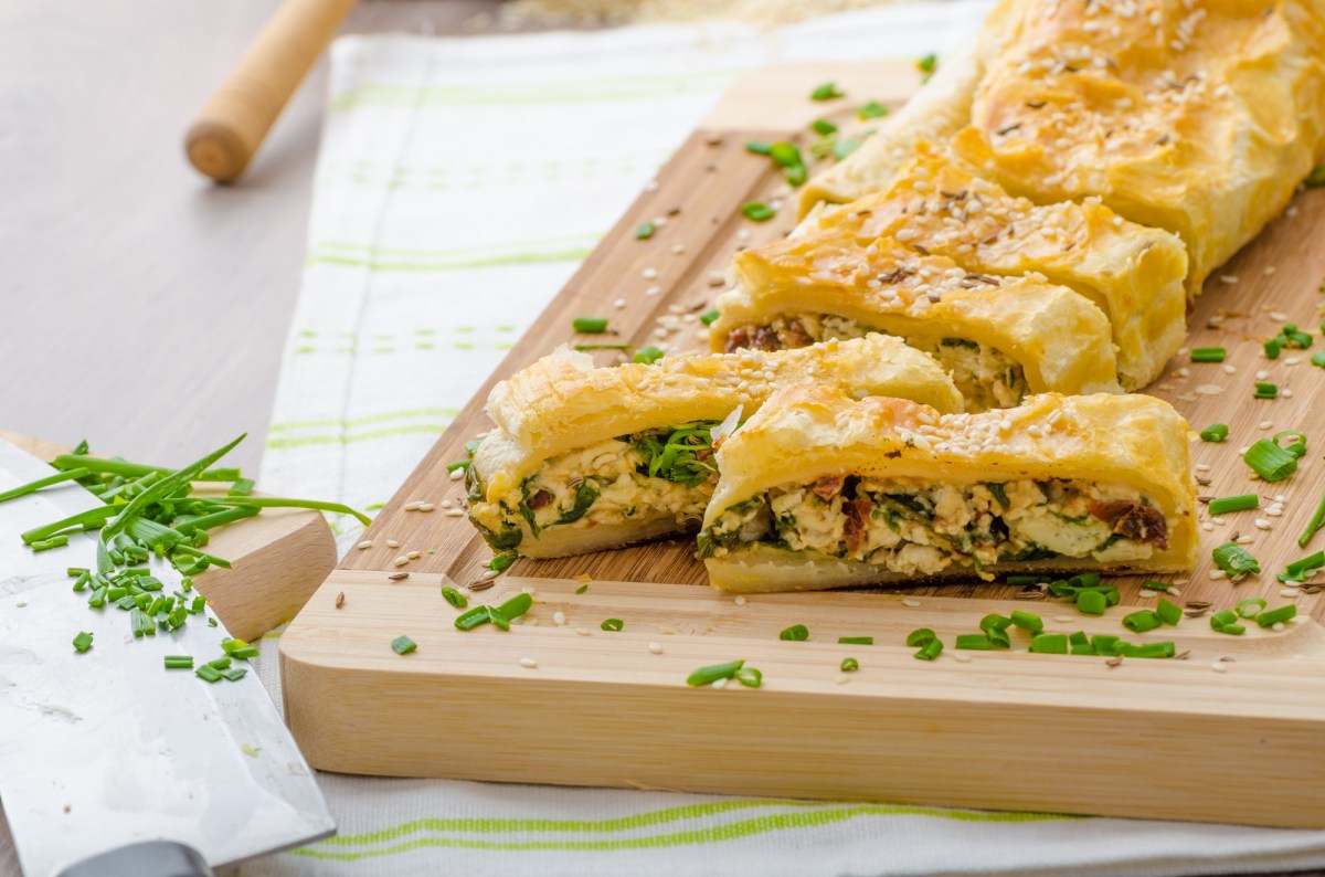 Brett mit angeschnittenem BlÃ¤tterteigstrudel mit Spinat und BlauschimmelkÃ¤se