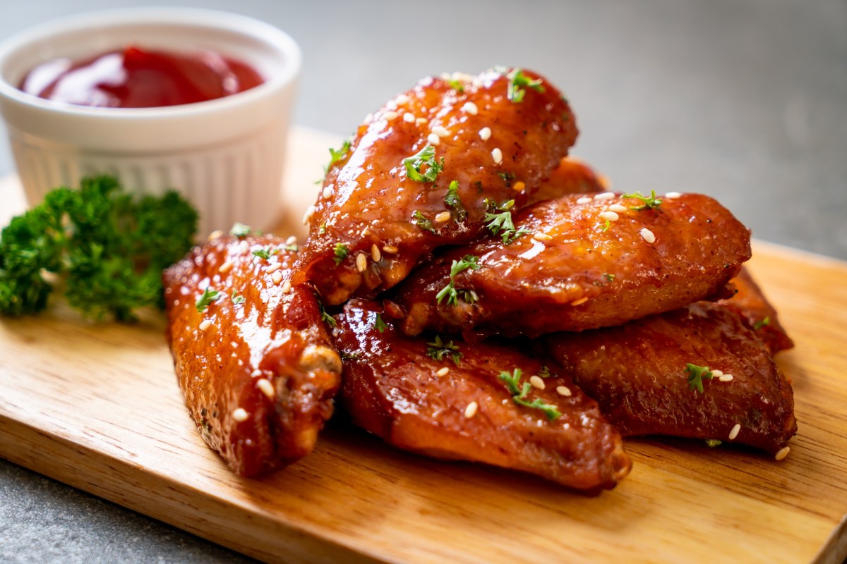 Ein paar Chicken Wings aus dem Airfryer aus einem Brett, bestreut mit Petersilie, daneben eine weiÃŸe Schale Ketchup.