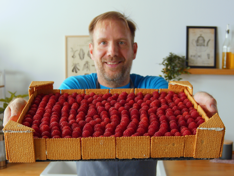 Ein Mann hÃ¤lt eine Himbeer-Buttercreme-Torte in die Kamera.