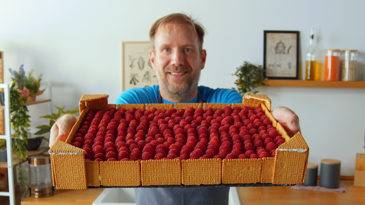 Ein Mann hÃ¤lt eine Himbeer-Buttercreme-Torte in die Kamera.