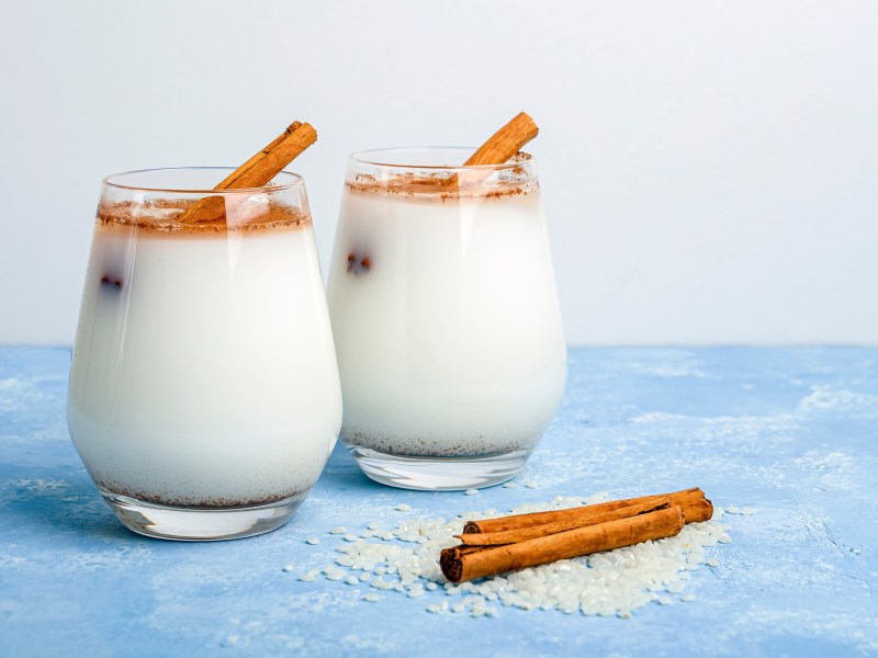 Zwei GlÃ¤ser Horchata auf einem blauen Tisch, garniert mit Zimt und Zimtstangen.