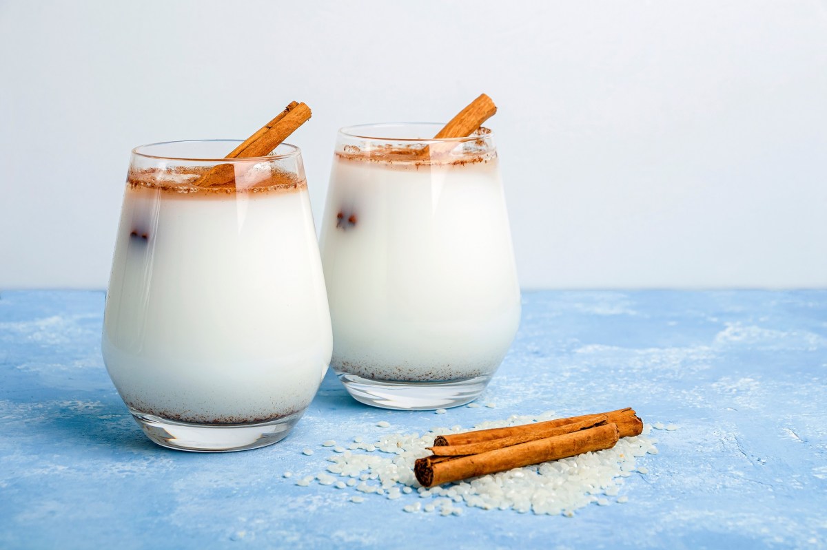 Zwei GlÃ¤ser Horchata auf einem blauen Tisch, garniert mit Zimt und Zimtstangen.