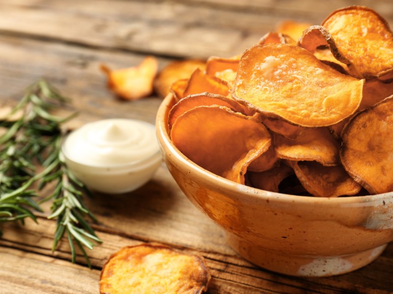 Eine SchÃ¼ssel KÃ¼rbis-Chips, daneben eine Schale mit weiÃŸem Dip und ein paar Rosmarinzweige.