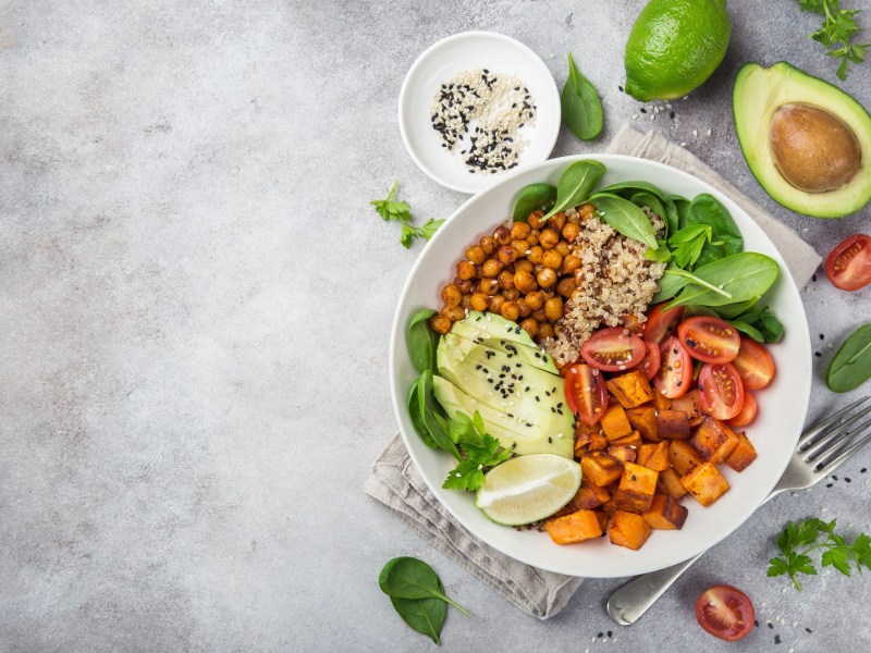 KÃ¼rbis-Quinoa-Bowl mit Kichererbsen und Avocado in der Draufsicht, drumherum Zutaten.