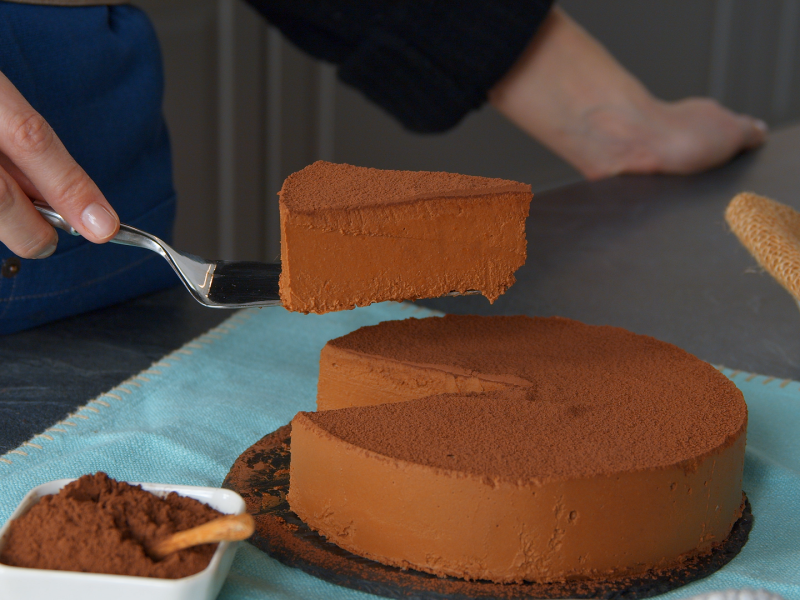 Eine Hand hebt ein StÃ¼ck KÃ¼rbis-Schokokuchen mit einem Tortenheber aus dem restlichen Kuchen.