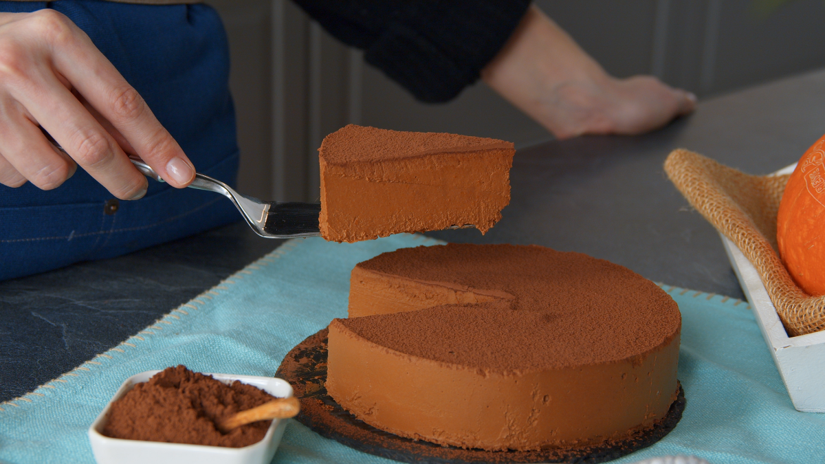 Eine Hand hebt ein StÃ¼ck KÃ¼rbis-Schokokuchen mit einem Tortenheber aus dem restlichen Kuchen.