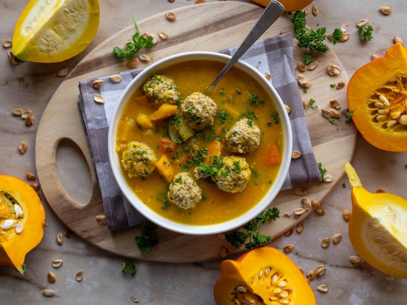 Eine SchÃ¼ssel KÃ¼rbissuppe mit HackbÃ¤llchen. Daneben liegen angeschnittene KÃ¼rbisse.