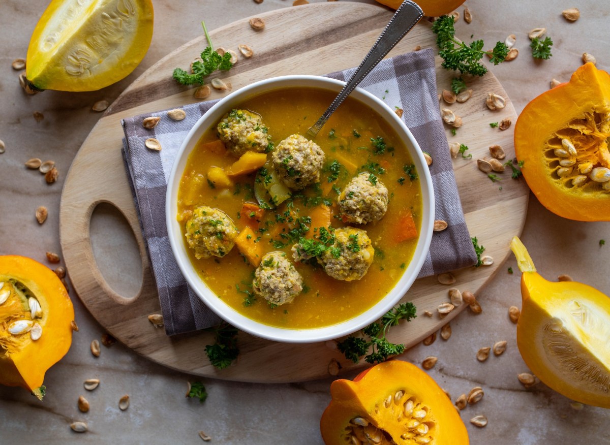 Eine SchÃ¼ssel KÃ¼rbissuppe mit HackbÃ¤llchen. Daneben liegen angeschnittene KÃ¼rbisse.