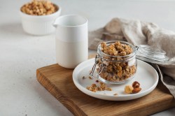 Ein Glas Müsli aus dem Airfryer auf einem Teller, drumherum ein paar Frühstücksutensilien.