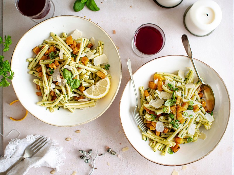 Zwei Teller Nudeln mit KÃ¼rbis und Pesto, serviert mit Parmesan.