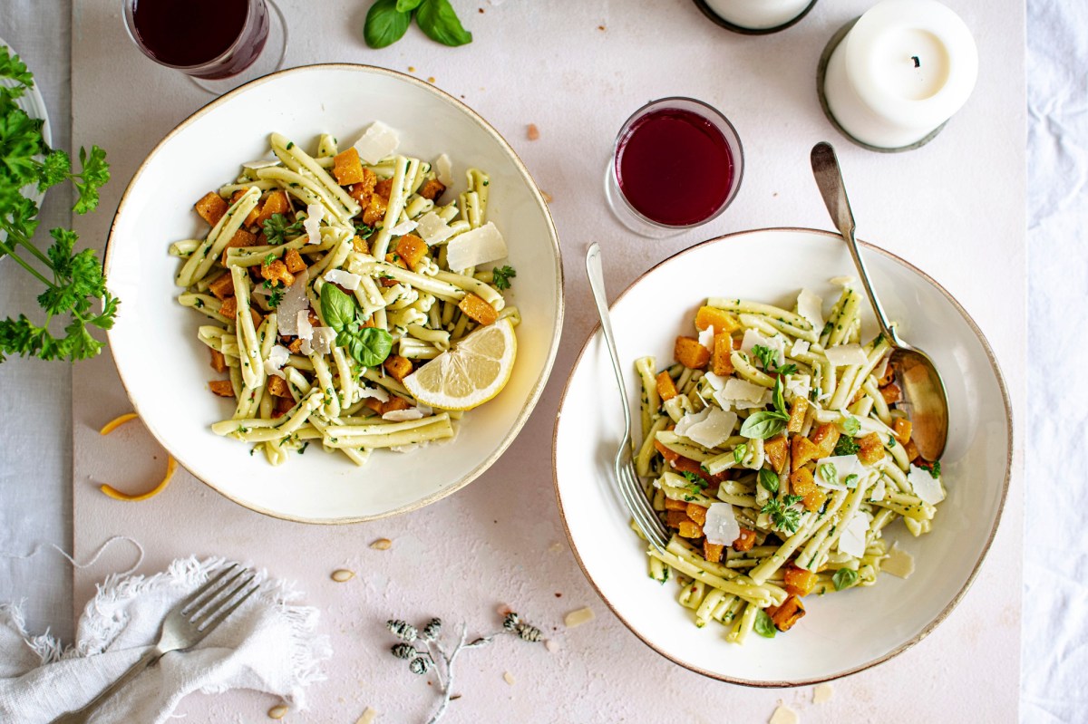 Zwei Teller Nudeln mit KÃ¼rbis und Pesto, serviert mit Parmesan.