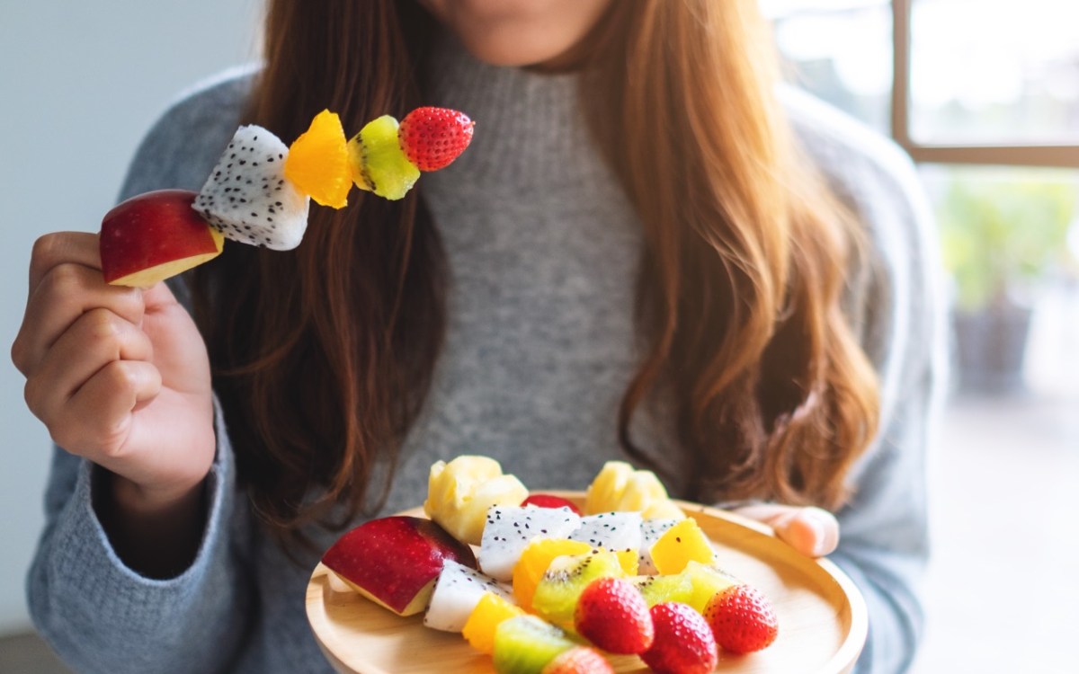 Obst am Abend essen: Eine Frau hÃ¤lt einen ObstspieÃŸ in der rechten und einen Teller mit ObstspieÃŸen in de rlinken Hand.