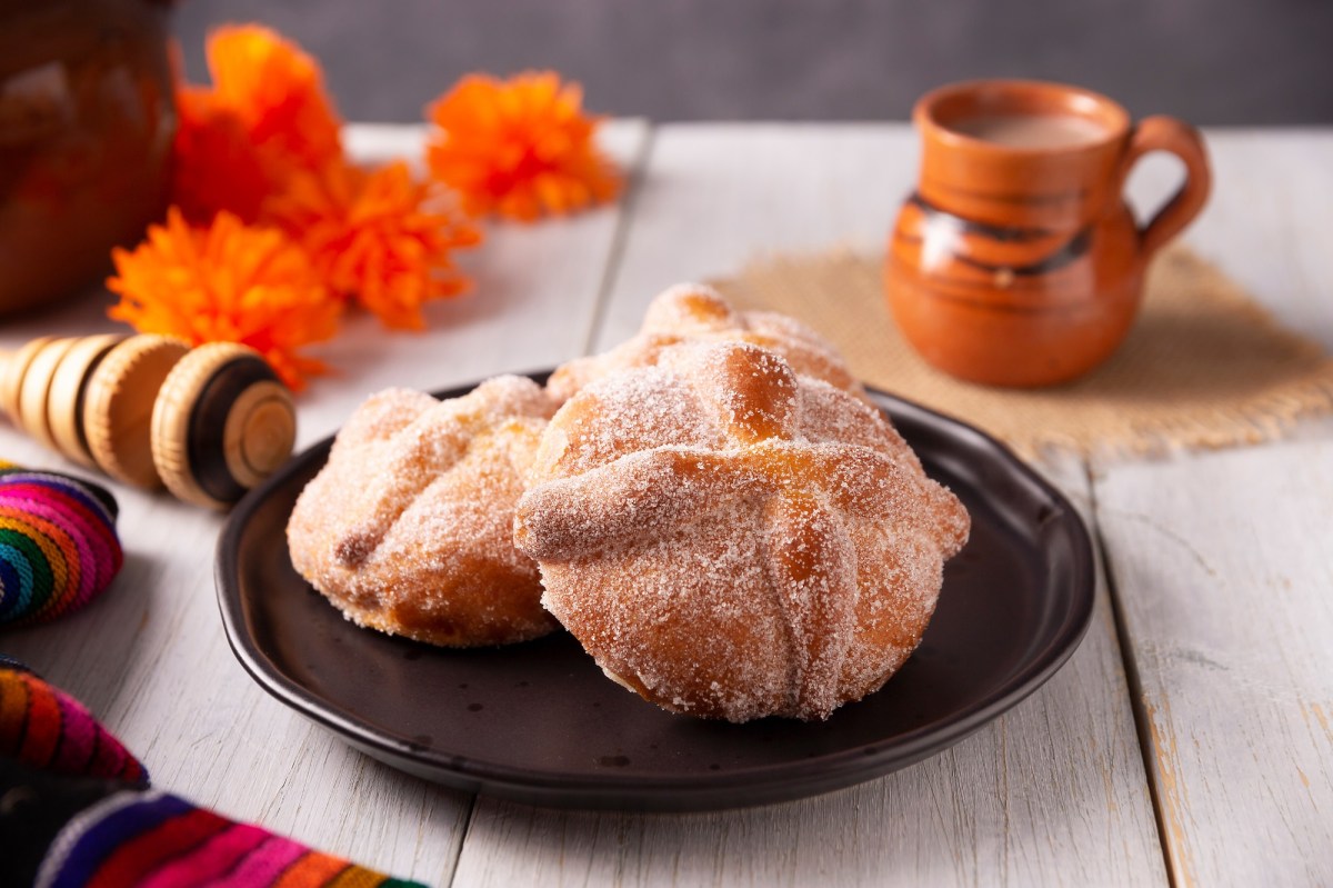 Pan de Muerto auf einem schwarzen Teller. Dahinter steht eine Tasse mit mexikanischer heiÃŸer Schokolade.