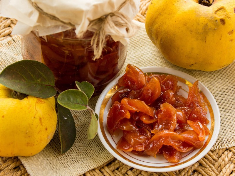 Ein Glas Quitten-Chutney, daneben ein Teller mit dem Chutney und zwei frische Quitten.