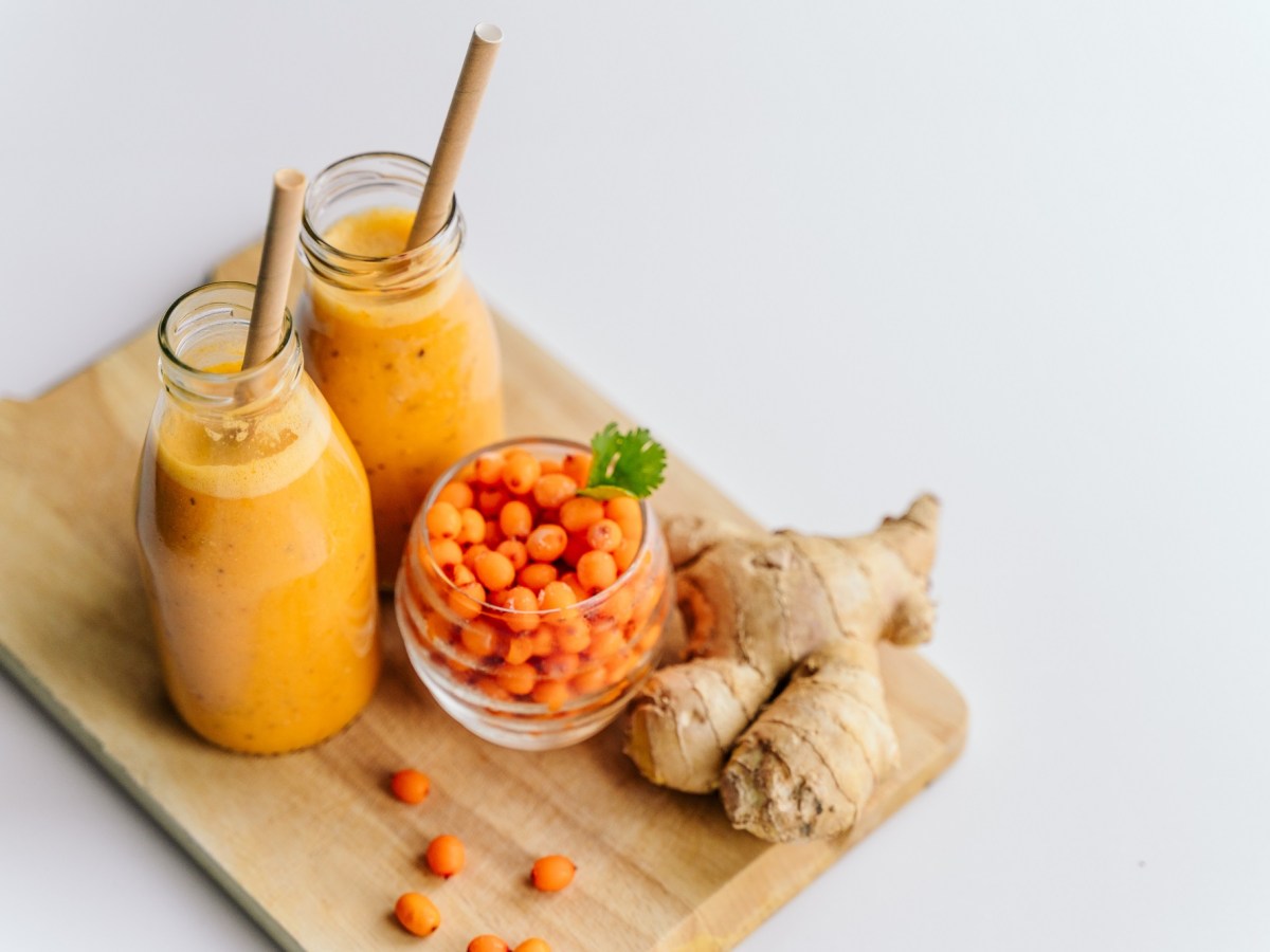 Zwei GlÃ¤ser Sanddorn-Ingwer-Smoothie mit Sanddornbeeren und Ingwer daneben