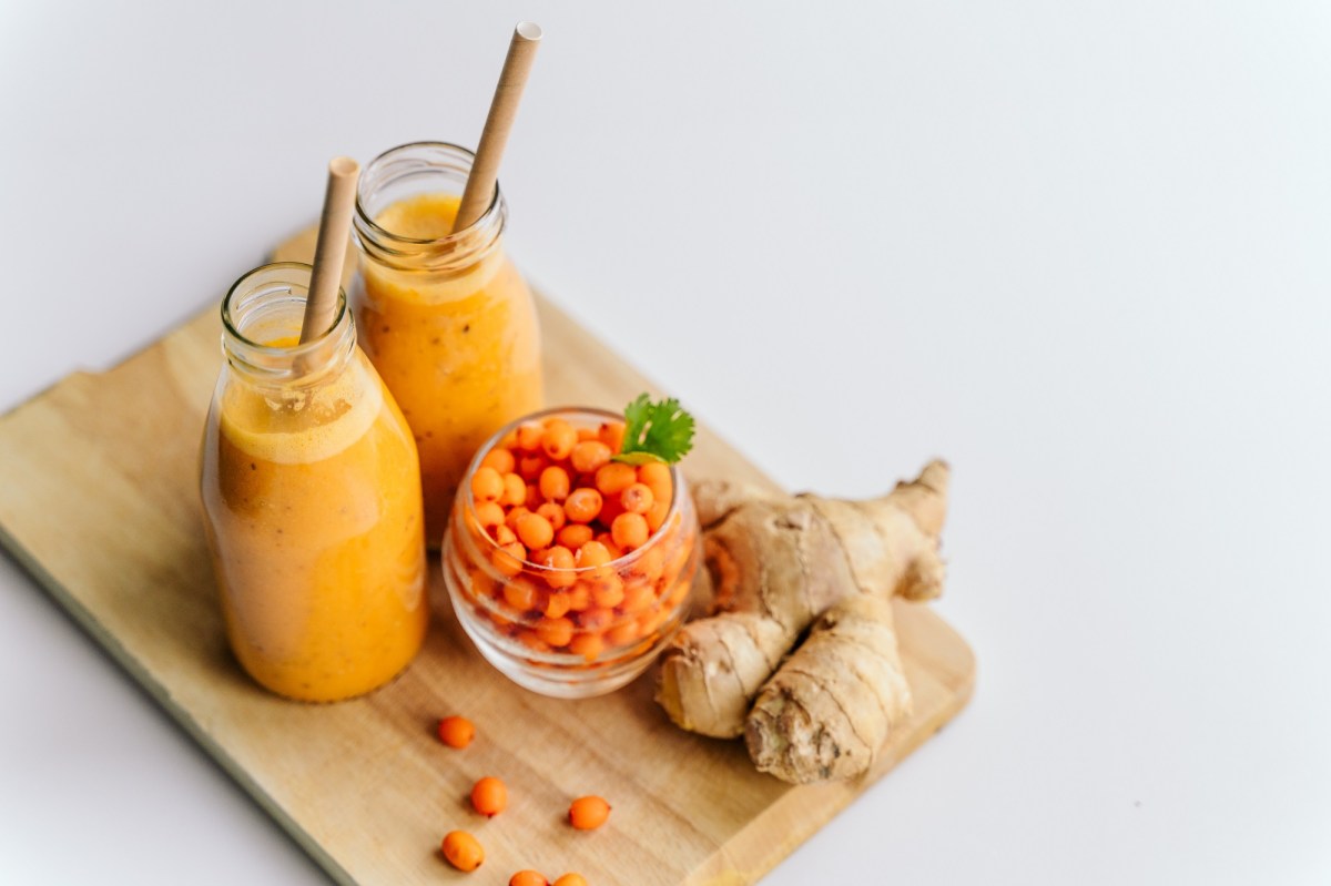 Zwei GlÃ¤ser Sanddorn-Ingwer-Smoothie mit Sanddornbeeren und Ingwer daneben