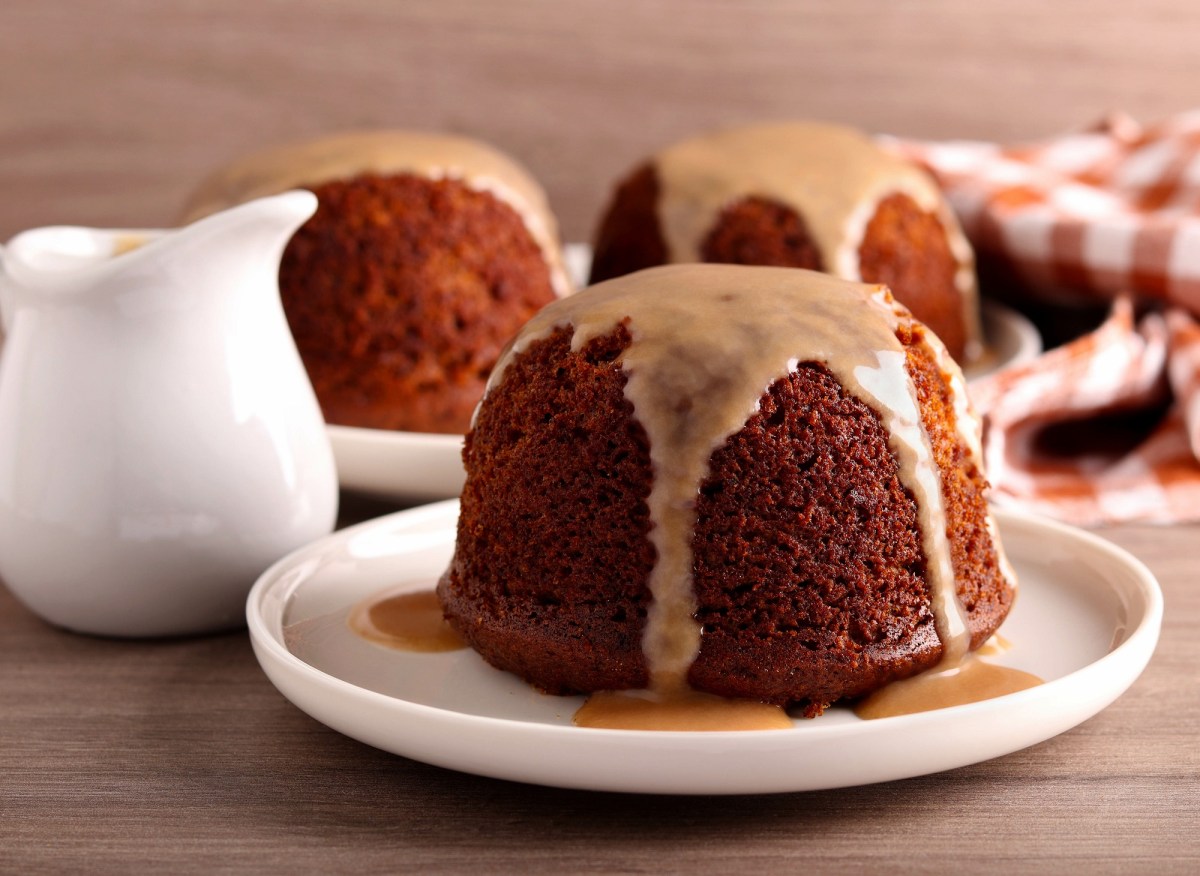 Sticky Toffee Pudding auf einem Teller, Ã¼bergossen mit KaramellsoÃŸe. Daneben steht ein KÃ¤nnchen mit SoÃŸe.