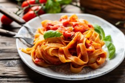 Ein Teller Tomaten-Creme-Pasta garniert mit Basilikum, daneben Besteck, Nahaufnahme.