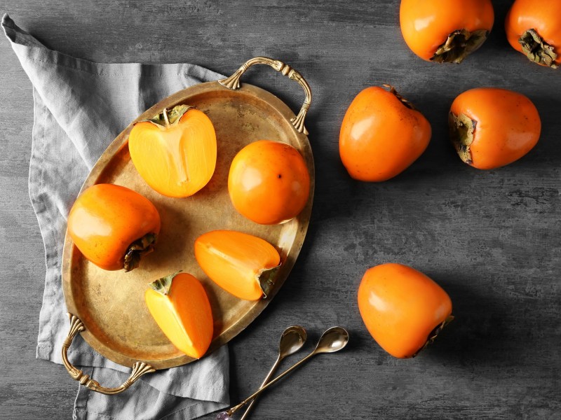 Unterschied Kaki, Sharonfrucht, Persimone: Einige angeschnittene FrÃ¼chte liegen auf einem Tablett.