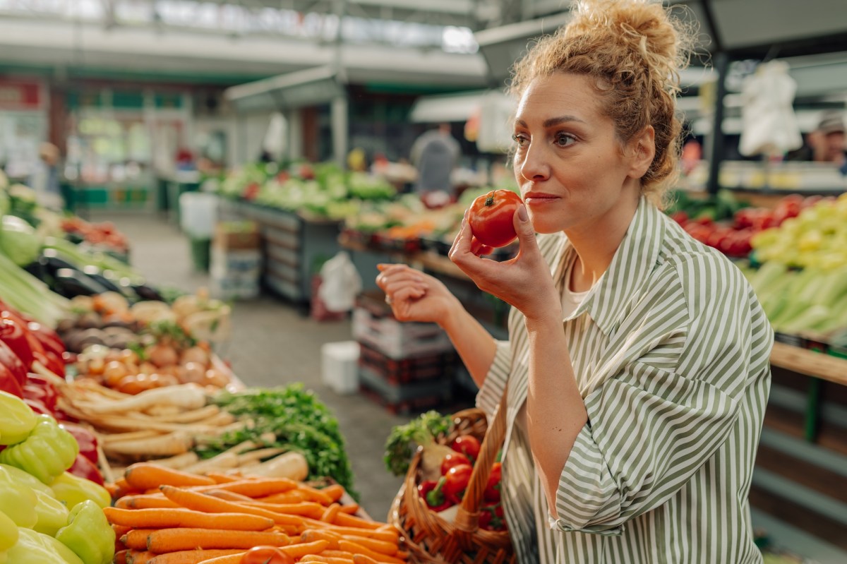 Vegane Mythen: eine Frau steht am Gemüsestand und hält eine Tomate in der einen und einen Einkaufskorb in der anderen Hand.