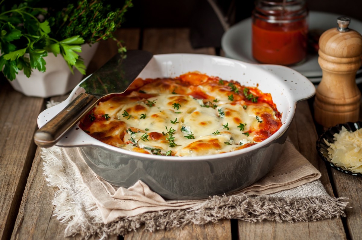 WeiÃŸkohl-Lasagne in runder Auflaufform auf einem Geschirrhandtuch, drumherum GewÃ¼rzstreuer, und KrÃ¤uter.