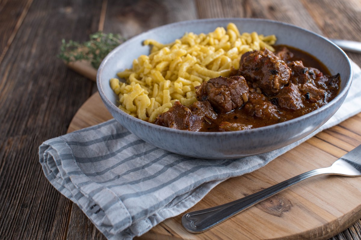 Ein Teller Wiener Saftgulasch mit SpÃ¤tzle auf einem Geschirrtuch.