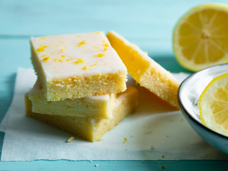 4 StÃ¼cke Zitronen-Brownies Lemonies auf Backpapier, daneben halbierte Zitronen.