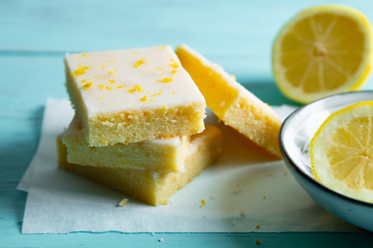 4 StÃ¼cke Zitronen-Brownies Lemonies auf Backpapier, daneben halbierte Zitronen.