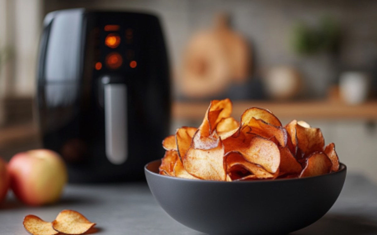 Apfelchips aus der HeiÃŸluftfritteuse in einer Schale. Im Hintergrund ist der Airfryer zu sehen.