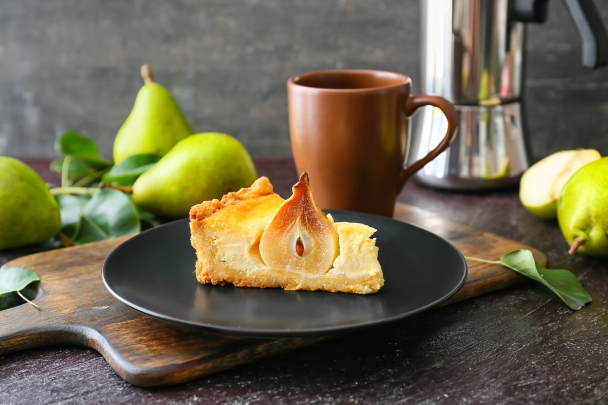 Ein StÃ¼ck Birnen-Schmand-Kuchen mit einer halben Birne auf einem dunklen Teller.