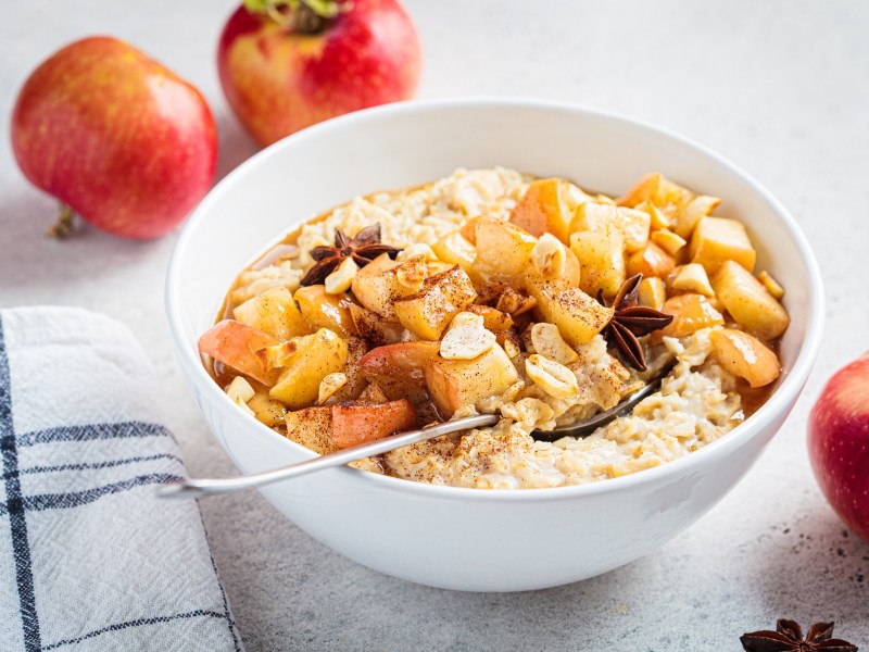 Eine Schale Bratapfel-Porridge mit gebratenen Ã„pfeln und Anissternen, drumherum Ã„pfel.