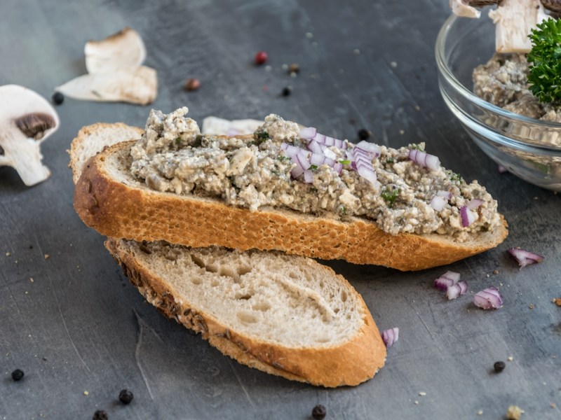 Scheibe Brot bestrichen mit Champignon-Zwiebel-Aufstrich und eine Schale mit dem Aufstrich dahinter