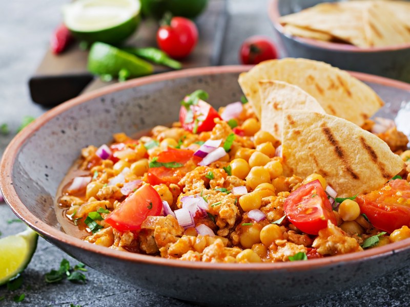 Eine ServierschÃ¼ssel mit Chili con Carne mit KÃ¼rbis und Tortillas.