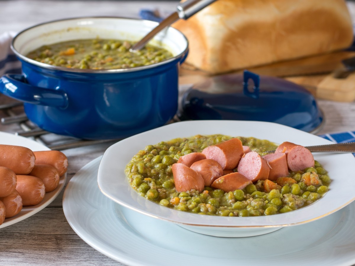 Ein Topf und ein Teller Erbsensuppe mit WÃ¼rstchen.