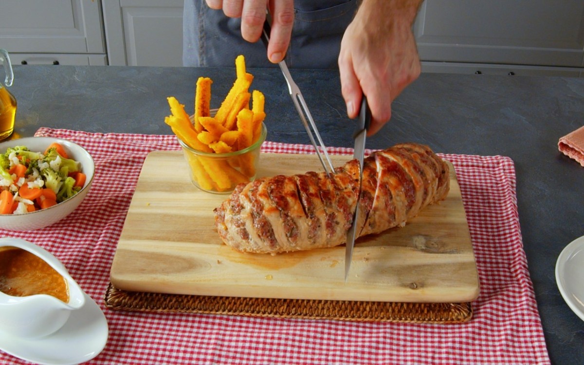 Ein gefÃ¼llter Schweinebraten wird mit einem Messer angeschnitten. Daneben Maispommes.