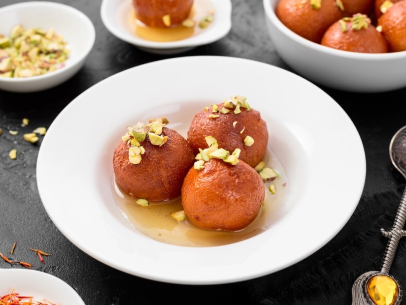 Gulab Jamun auf einem Teller mit gehackten Pistazien und Zuckersirup.