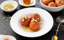 Gulab Jamun auf einem Teller mit gehackten Pistazien und Zuckersirup.