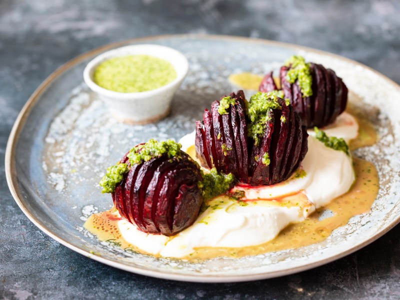 3 Hasselback-Rote-Beten auf einem Teller, garniert mit KrÃ¤utersoÃŸe und Joghurt.