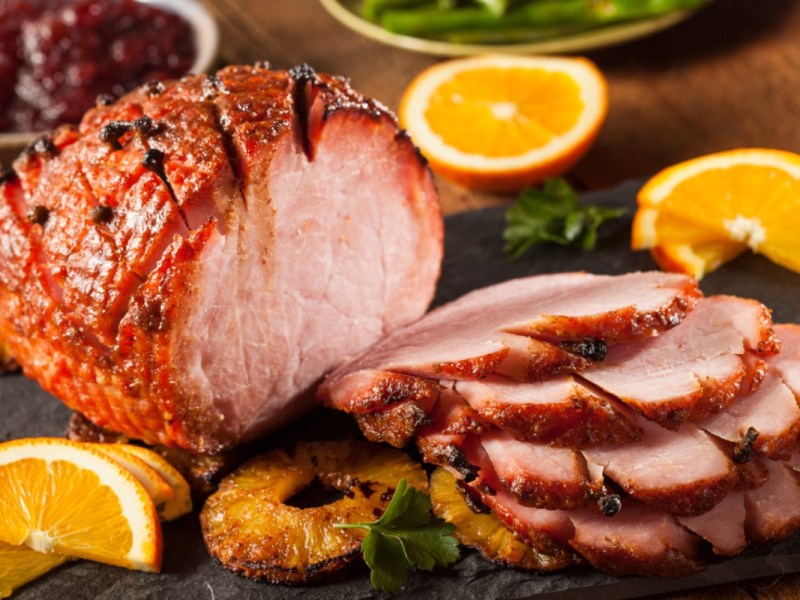 Ein Honey Glazed Ham mit karamellisierten Ananasscheiben, der zur Hälfte in Scheiben geschnitten wurde.